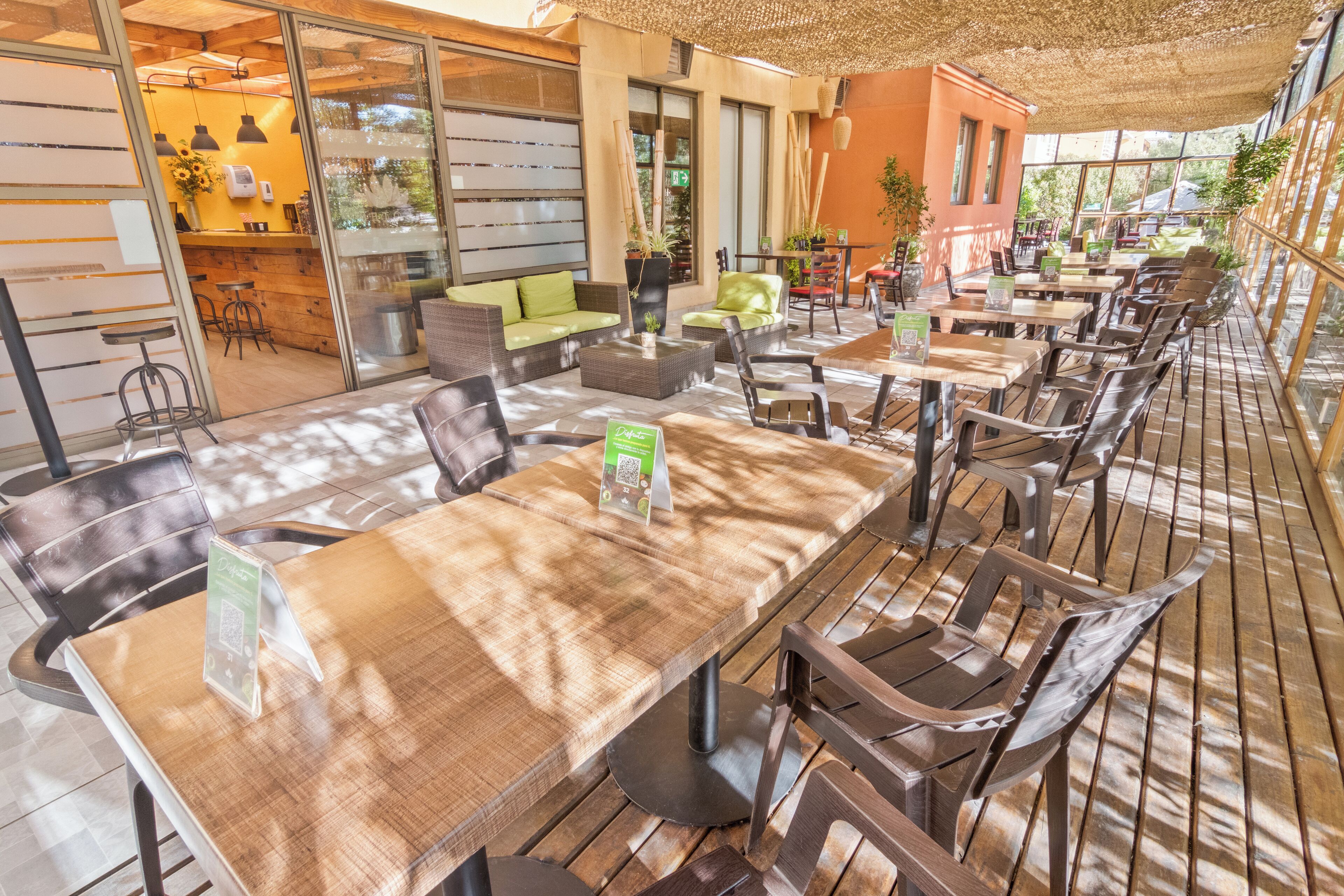 Un cafè a l'aire lliure amb taules i cadires de fusta, un sofà i una zona de bar.