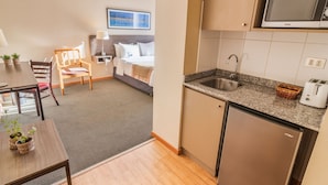 A compact hotel room with a kitchenette, a dining area with a table and chairs, a bed, and a small seating area. - Geotel Calama (Calama)