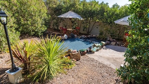 A backyard with a swimming pool, surrounded by rocks and plants, and two umbrellas providing shade. - Geotel Calama (Calama)