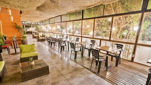 A spacious indoor area with multiple seating arrangements, including tables and chairs, and large windows offering a view of greenery outside. - Geotel Calama (Calama)