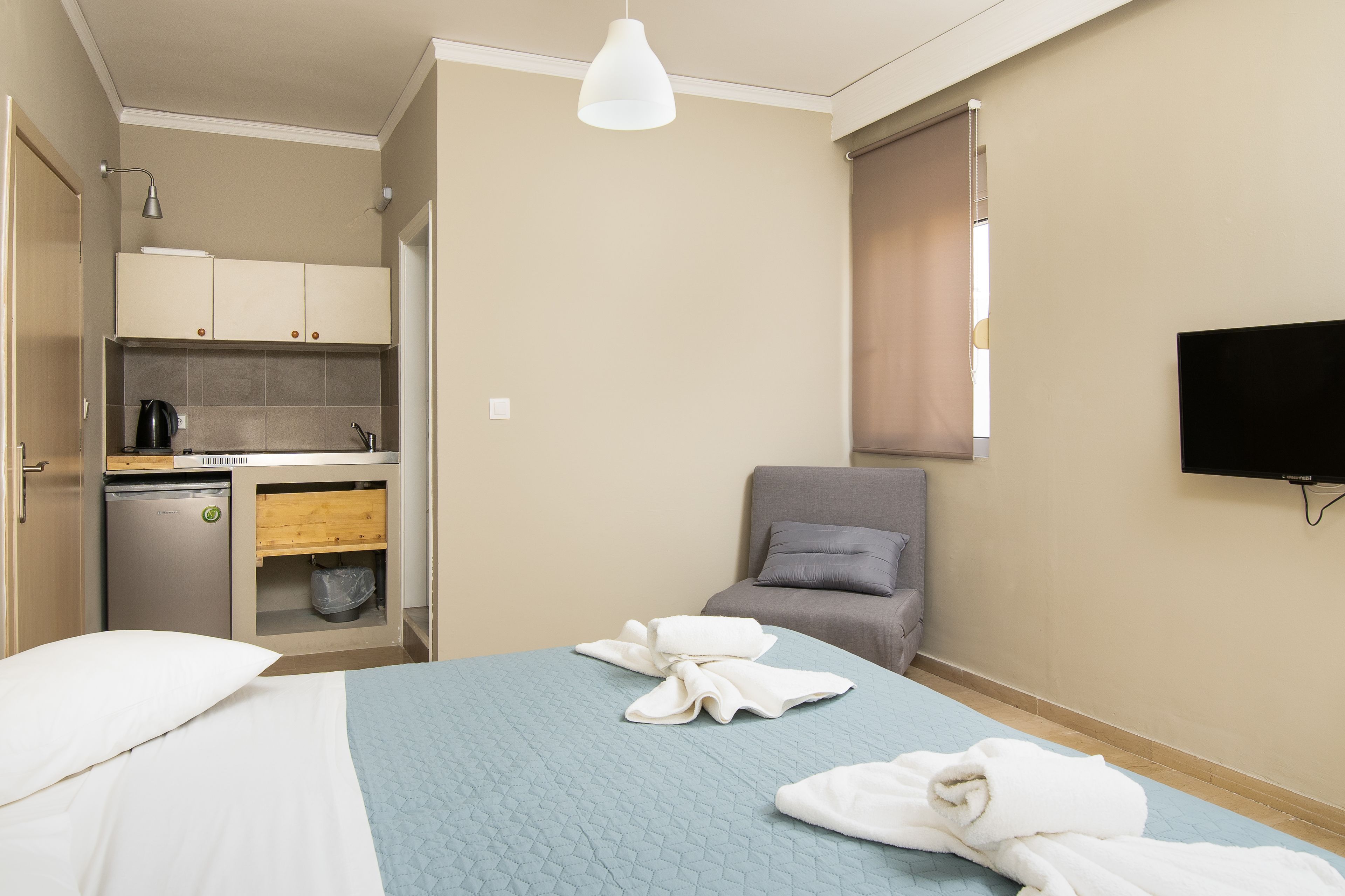 A hotel room with a bed, a chair, a TV, a kitchenette, and a window.
