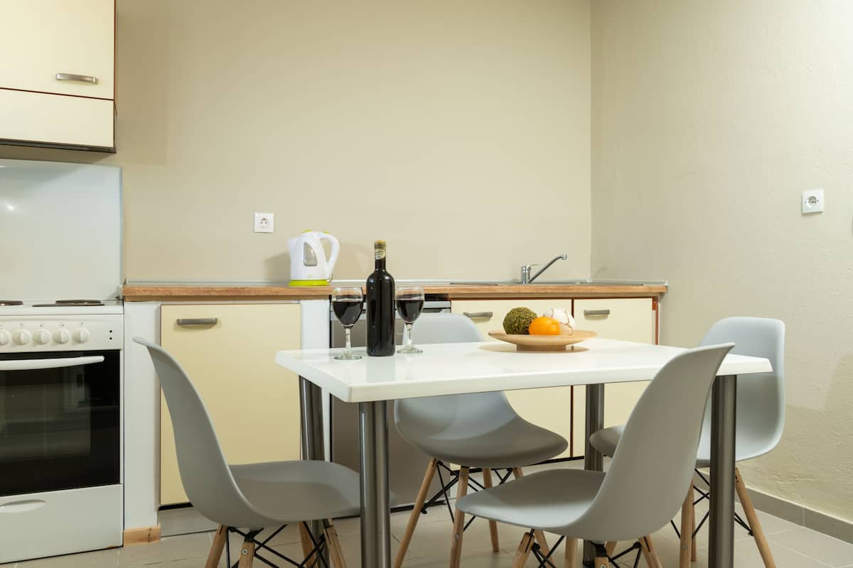 Eine kompakte Küche mit weißer Arbeitsplatte, einem eingebauten Backofen, einer Spüle und einem Essbereich mit weißem Tisch und vier grauen Stühlen.