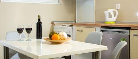 A compact kitchen with a dining table, chairs, a refrigerator, a dishwasher, and a window with a view of greenery.