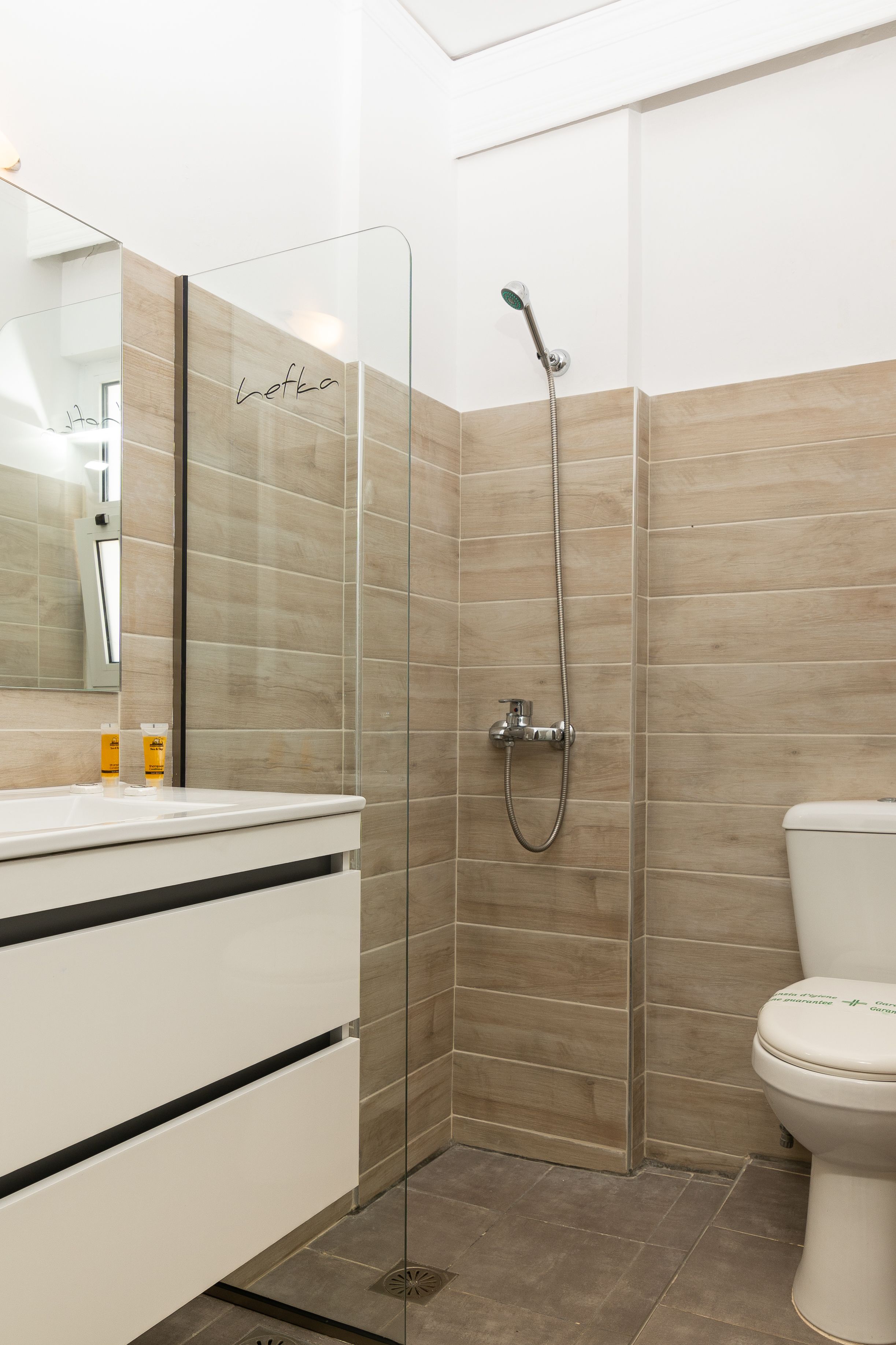 A modern bathroom with a glass shower enclosure, a white sink with black stripes, and a toilet with a green label.