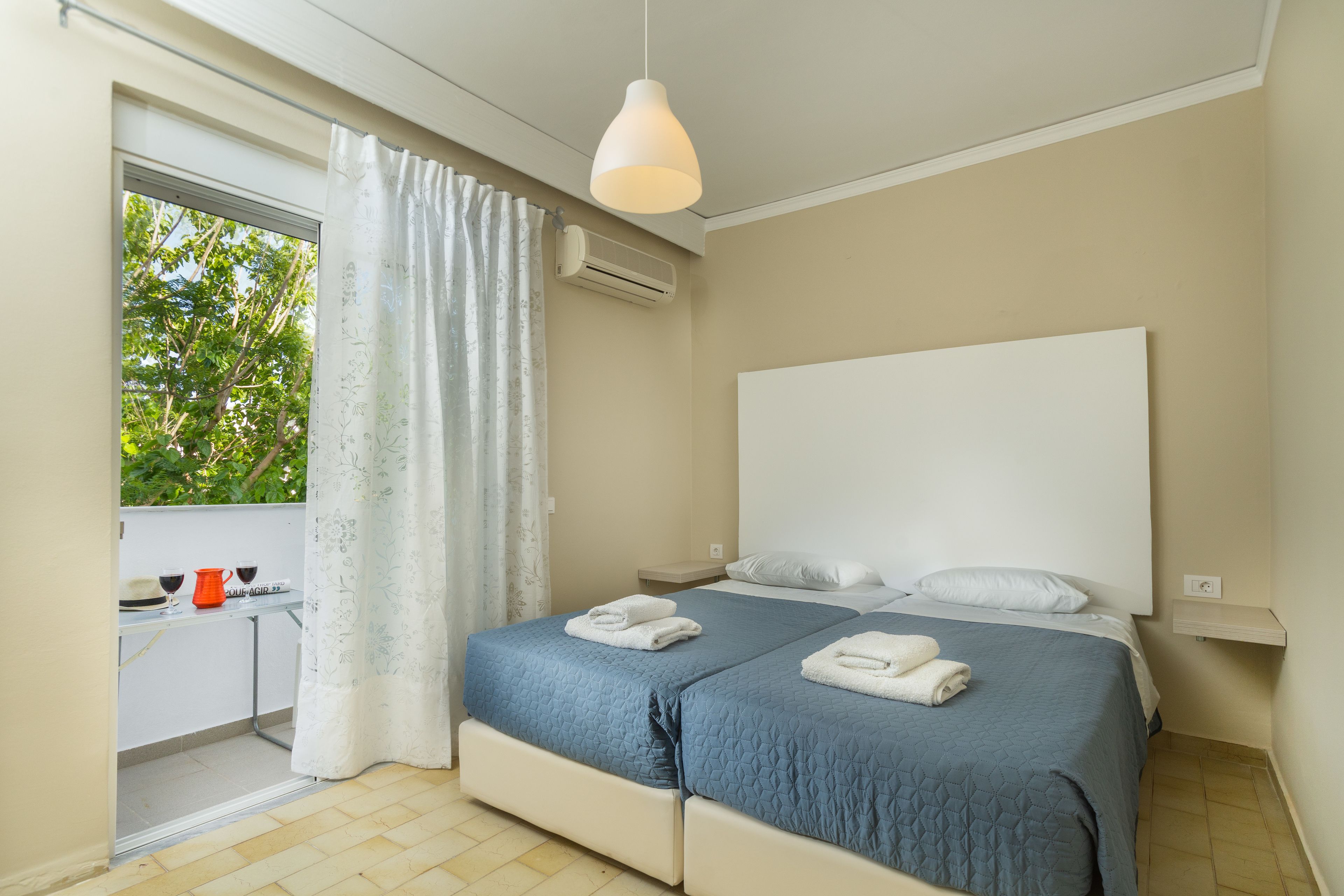 Ein Schlafzimmer mit zwei Betten, einem Fenster mit Vorhängen, einem Schreibtisch mit Stuhl und einer Klimaanlage.