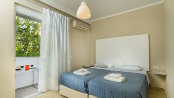 A bedroom with two beds, a window with curtains, a desk with a chair, and an air conditioning unit.
