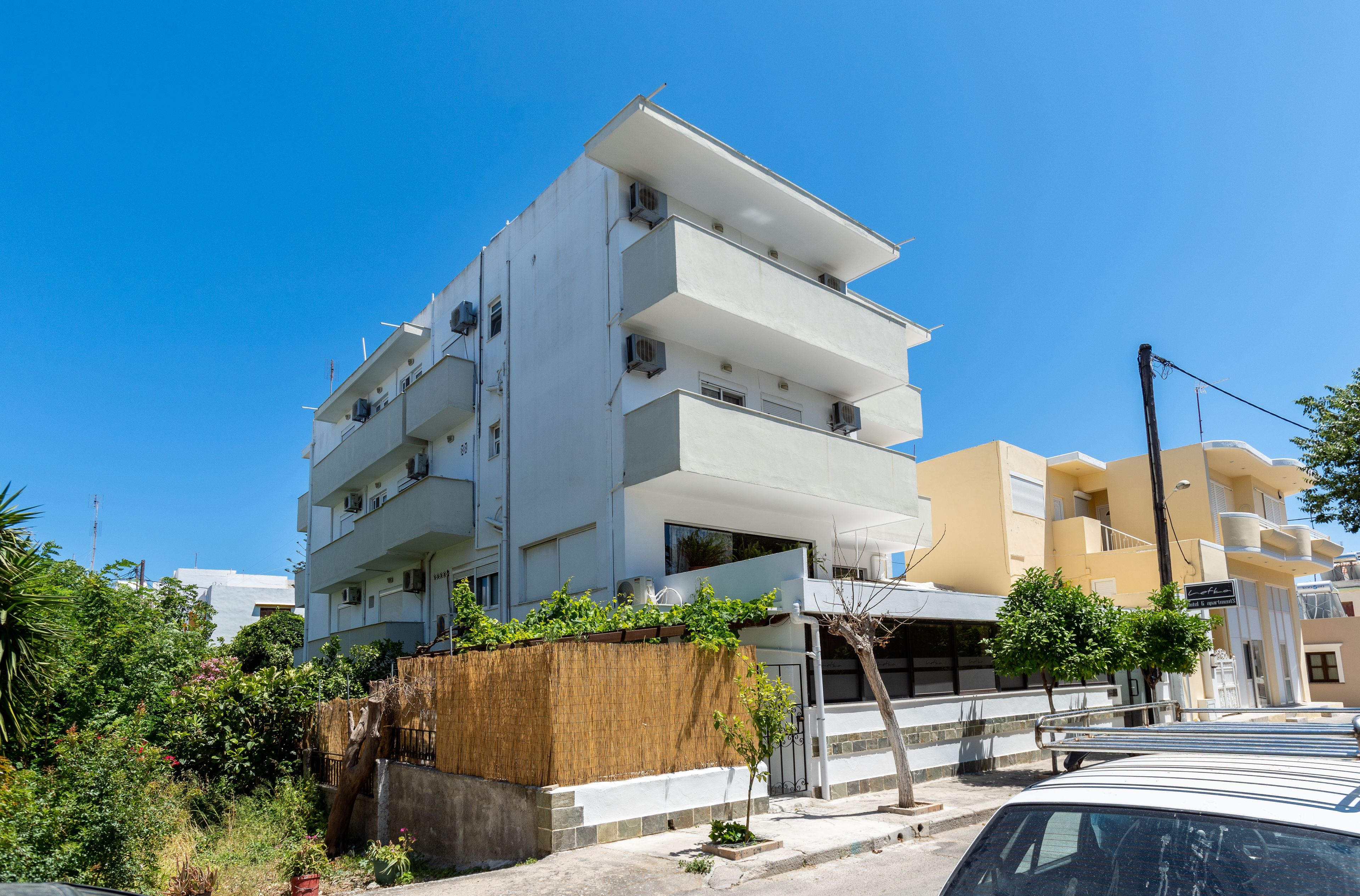 A modern multi-story building with balconies, a covered entrance, and a parking area.