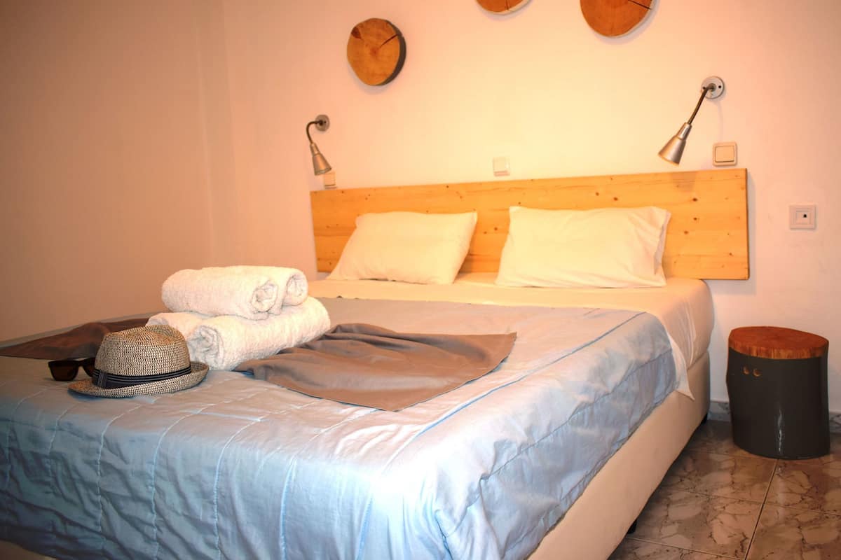 Ein ordentlich gemachtes Bett mit Holz-Kopfteil, zwei Nachttischlampen und einer runden Wanduhr.