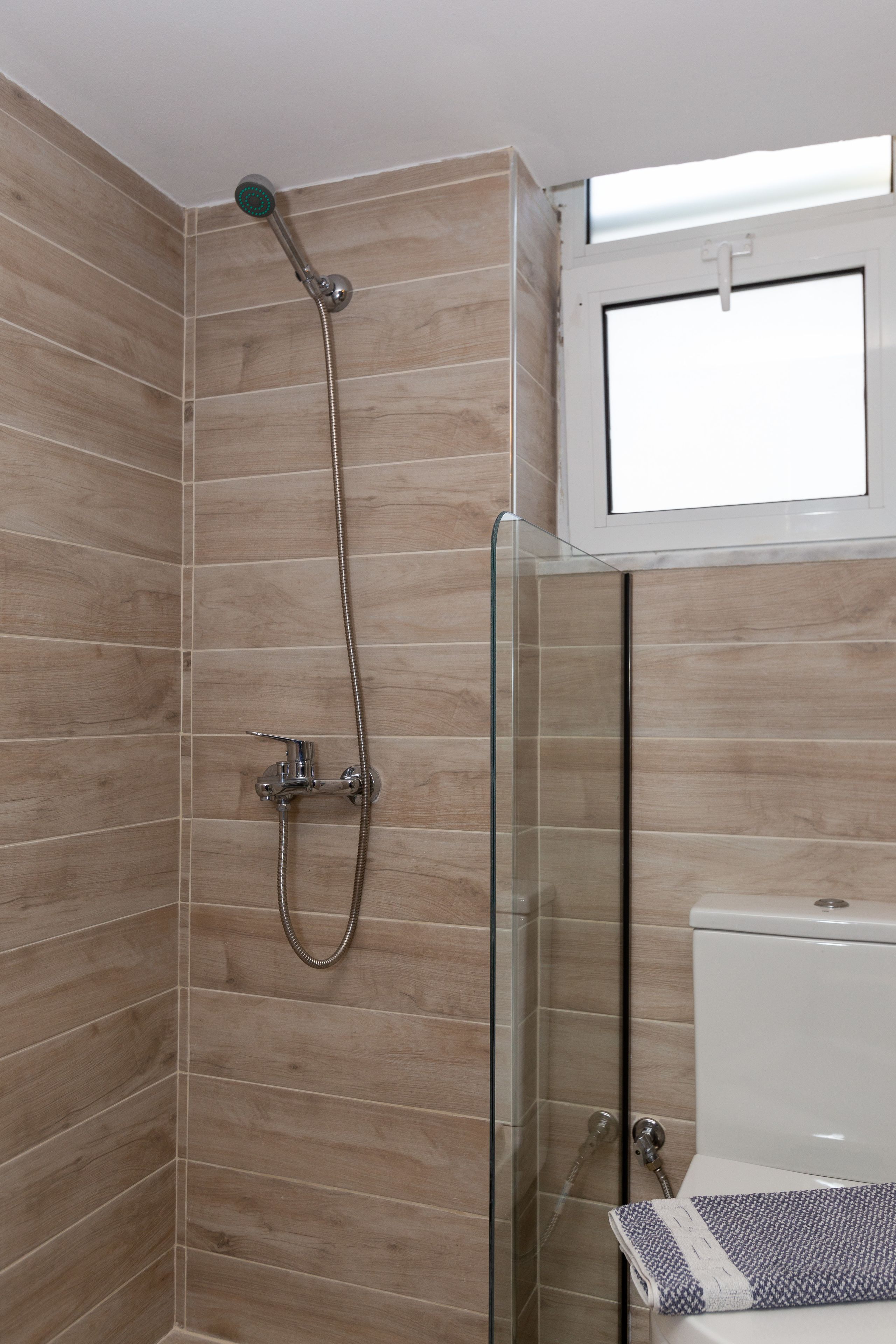 A bathroom with a glass shower enclosure, a toilet, and a window above the toilet.