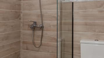Een badkamer met een douchecabine van glas, een toilet en een raam boven het toilet.