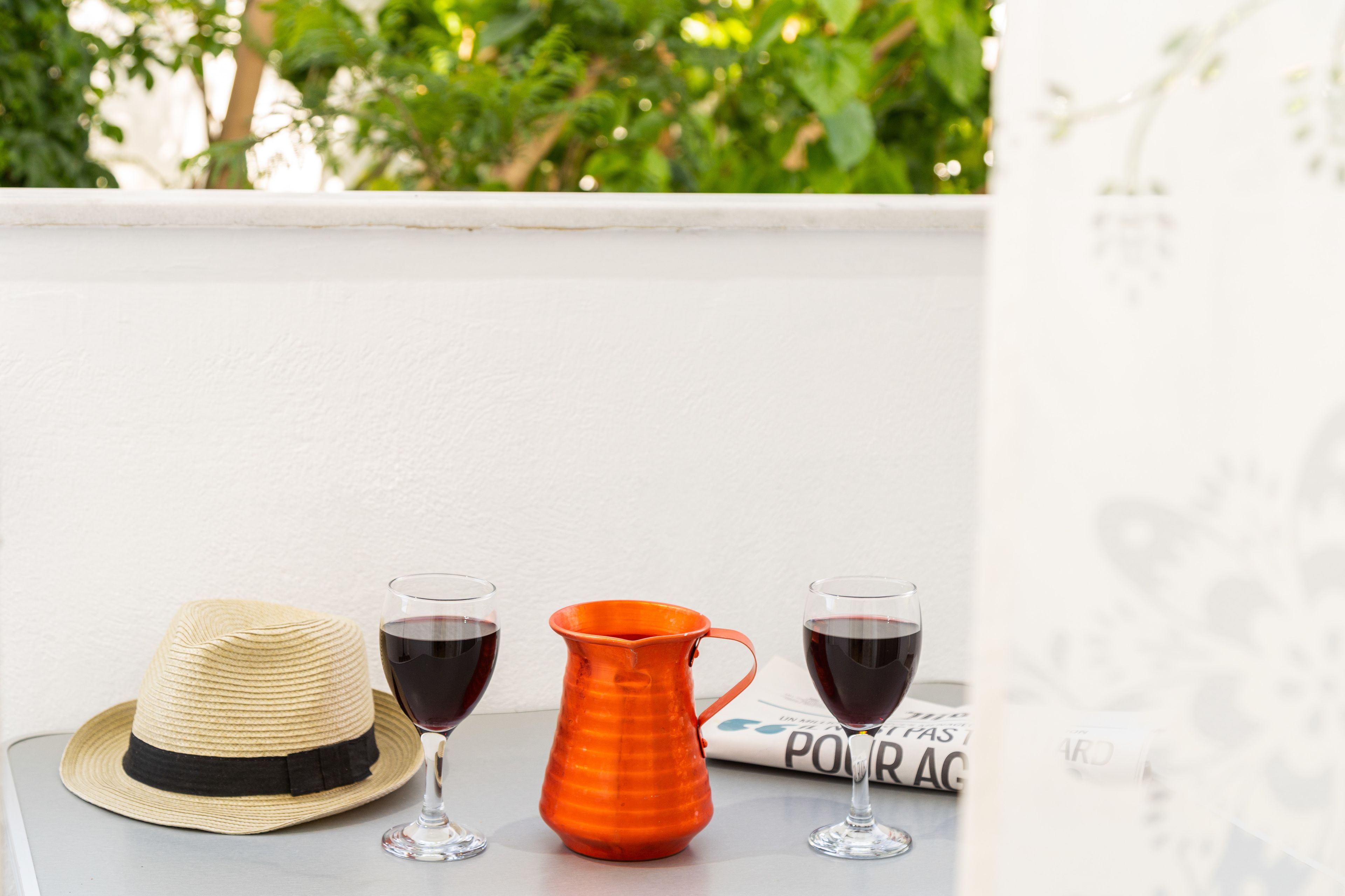 A table with a straw hat, two wine glasses, and an orange pitcher.