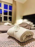 Una cama bien tendida con una toalla blanca enrollada, una colcha estampada y una ventana con cortinas.