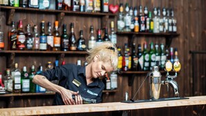 A bartender at a bar with a wooden interior and shelves stocked with various liquor bottles.
