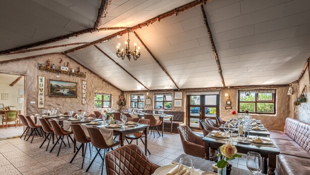 A restaurant with a rustic interior, featuring exposed wooden beams, a chandelier, and a variety of seating options including tables and a sofa.