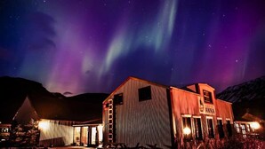 A rustic building with a sign reading "Anna" under a night sky with aurora borealis.