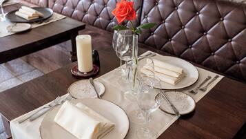Une table à manger dressée avec des assiettes, des couverts et une bougie, et un vase contenant une rose.