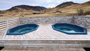 A wooden deck with two hot tubs overlooking a mountainous landscape.