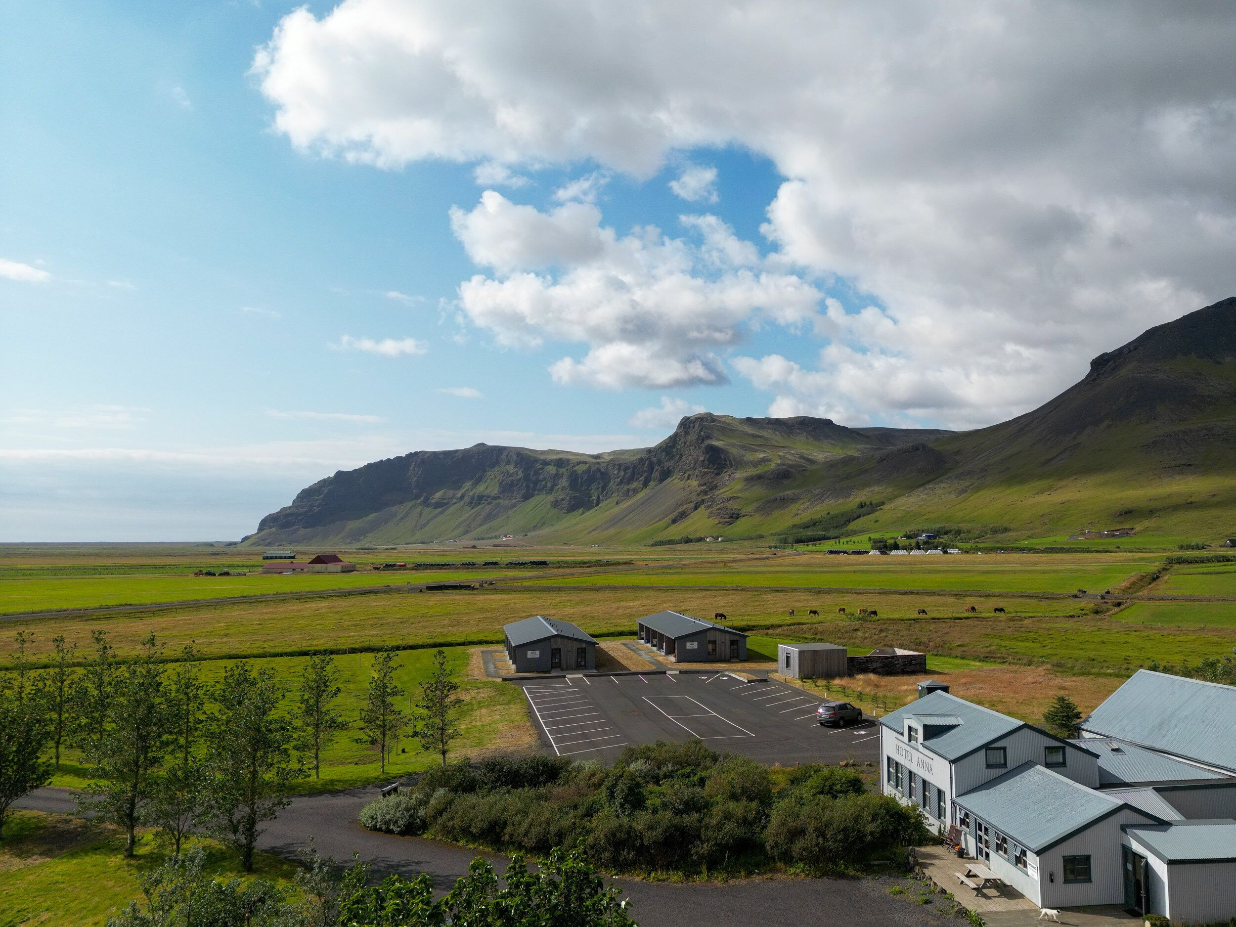 A hotel with a parking lot, surrounded by green fields and mountains.