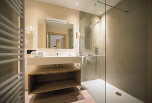 Un baño moderno con ducha envuelta en vidrio, tocador de madera y un espejo grande sobre el lavabo.