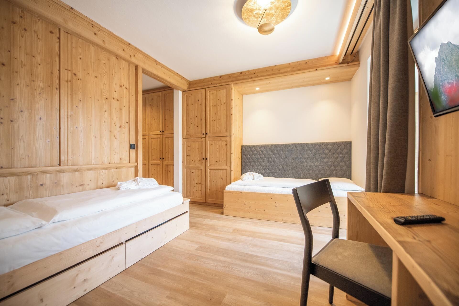 Une chambre d’hôtel avec des murs en bois, un lit doté d’une tête de lit grise, un bureau avec une chaise et un téléviseur fixé au mur.