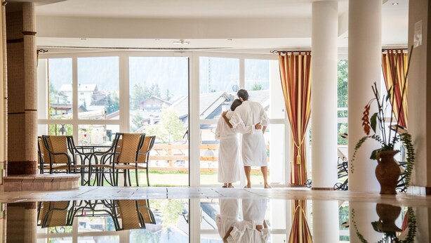 Una habitación amplia con ventanas grandes, una zona de comedor con sillas de mimbre y un suelo reflectante.