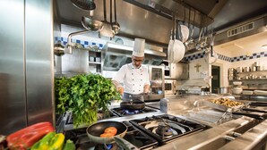 Un chef cocina en una cocina industrial con electrodomésticos de acero inoxidable y una variedad de verduras sobre la encimera.