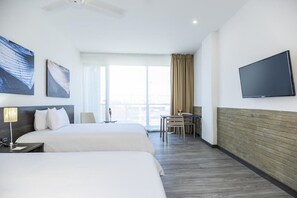 Habitación de hotel con dos camas, un escritorio, una silla, un televisor y un ventanal con cortinas.