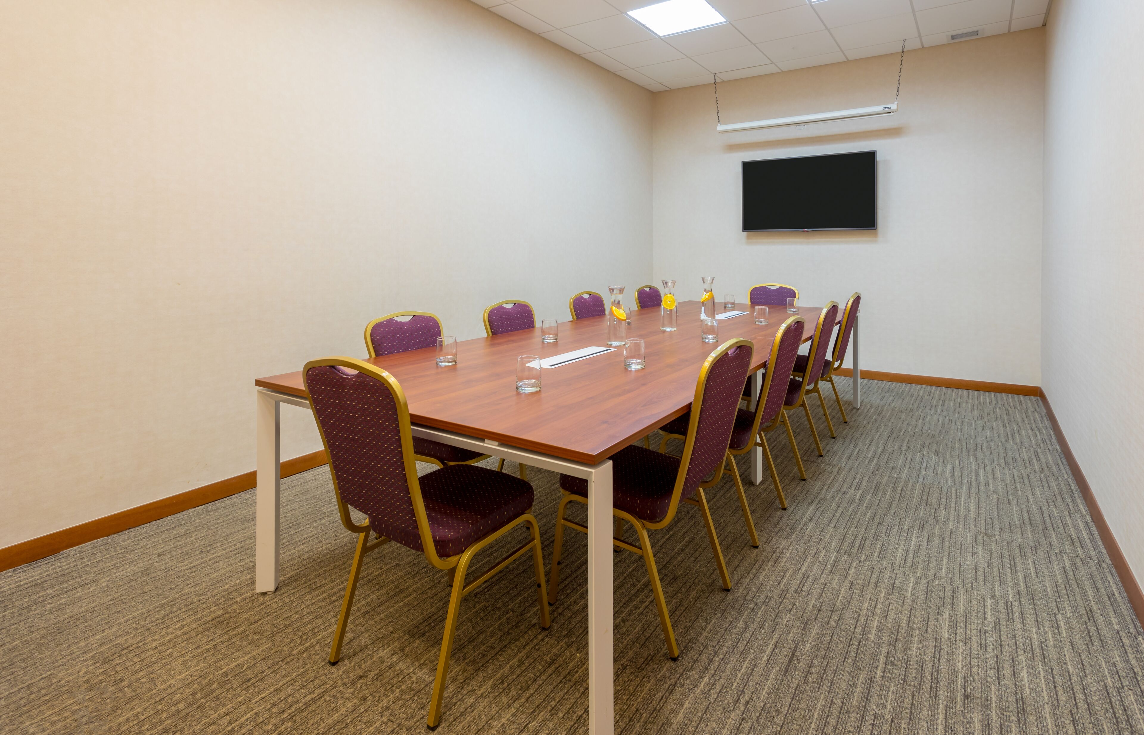 Een vergaderzaal met een lange tafel, paarse stoelen en een projectorscherm aan de muur.