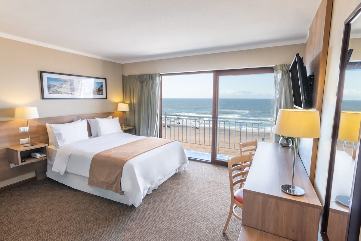 Een hotelkamer met een bed, bureau en uitzicht op de oceaan.