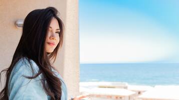 A person standing by a window overlooking a beach with a clear sky.