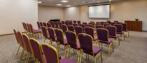 A conference room with rows of purple chairs and a projector screen.