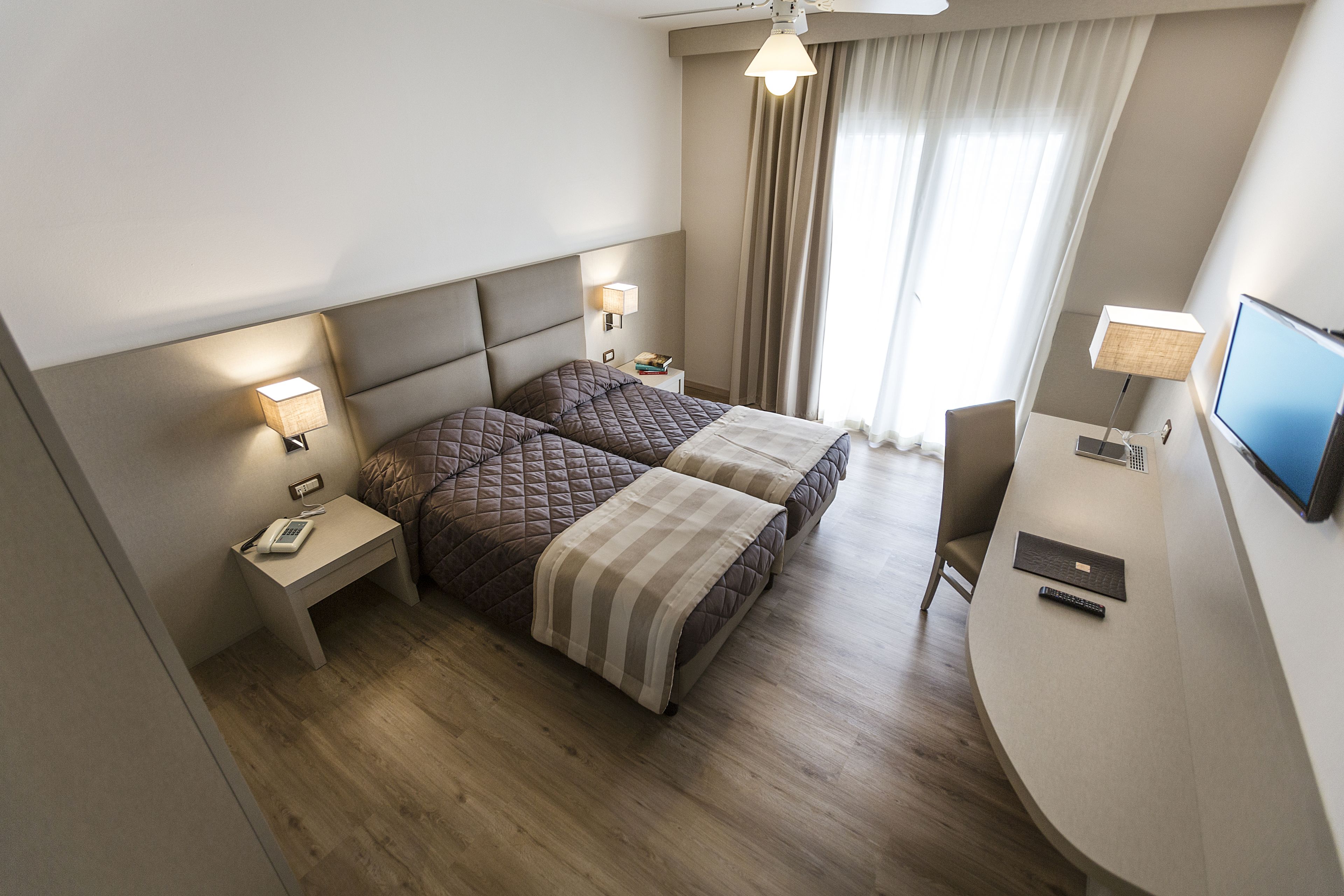 Una habitación de hotel con cama, mesitas de noche, escritorio, silla y televisión.