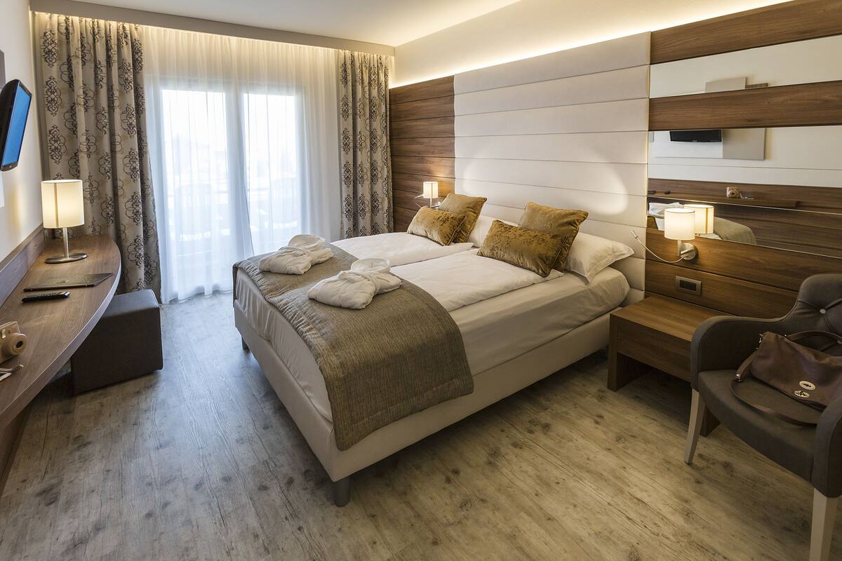 A modern hotel room with a large bed, bedside tables, a desk, and a chair.