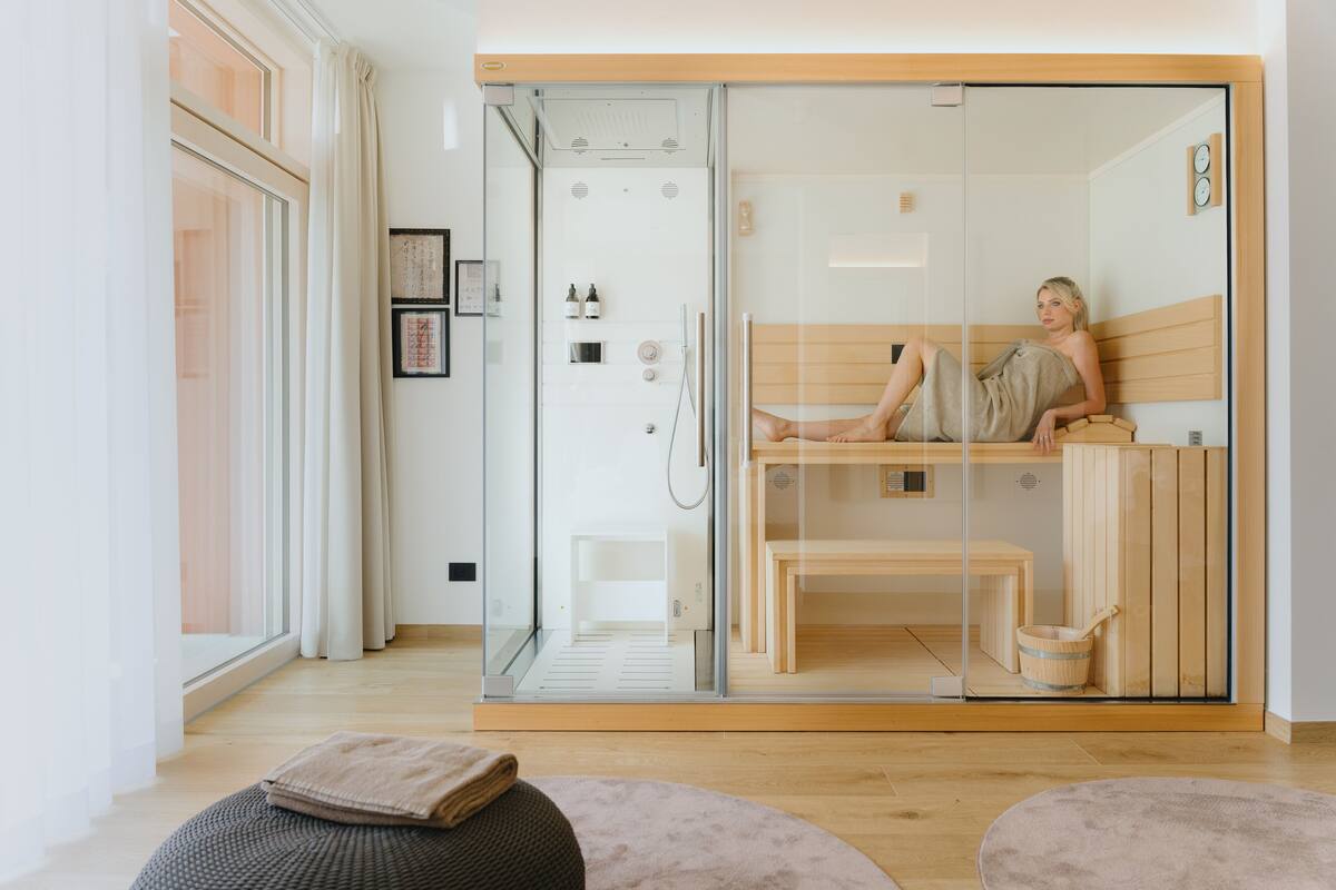 A modern spa room with a glass-enclosed sauna, wooden benches, and a visible sauna door.