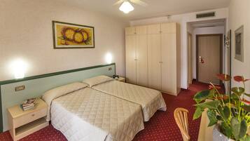 Habitación de hotel con dos camas, una mesita de noche, un armario, un ventilador de techo, un cuadro y una planta en maceta.