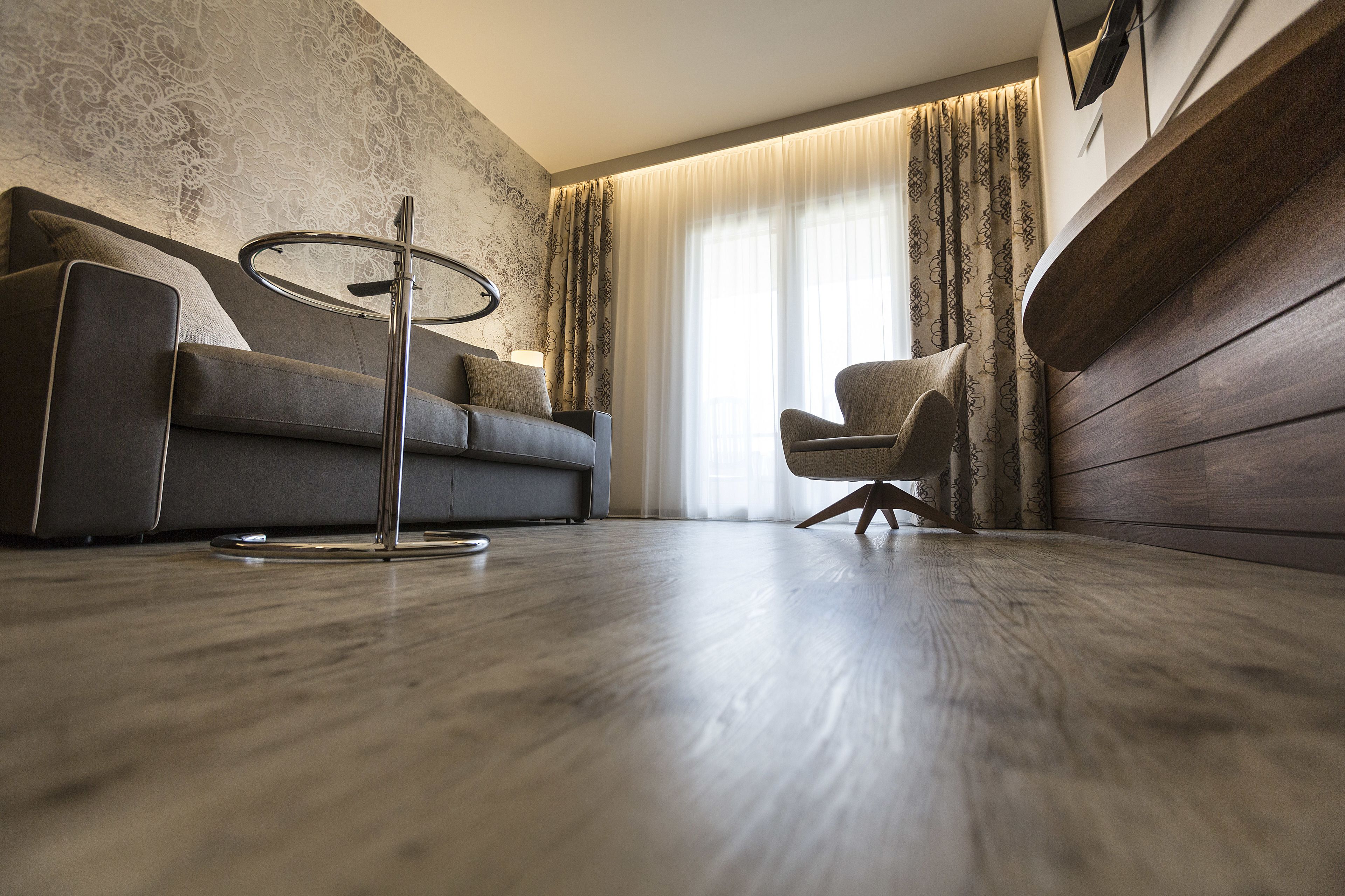 En moderne stue med sofa, stol, sofabord og et stort vindue med gardiner.