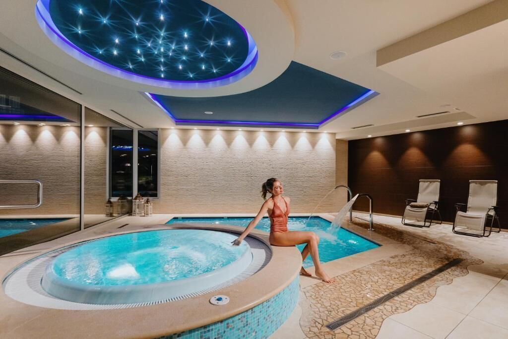 A modern indoor pool area with a hot tub, lounge chairs, and a ceiling with a starry light design.
