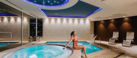 A modern indoor pool area with a hot tub, lounge chairs, and a ceiling with a starry light design.