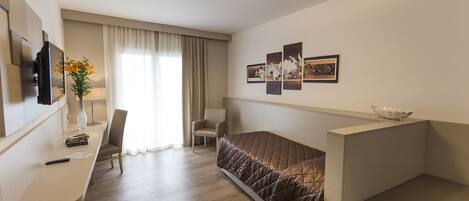 A hotel room with a bed, a desk, a chair, a TV, a vase with flowers, and a window with curtains.