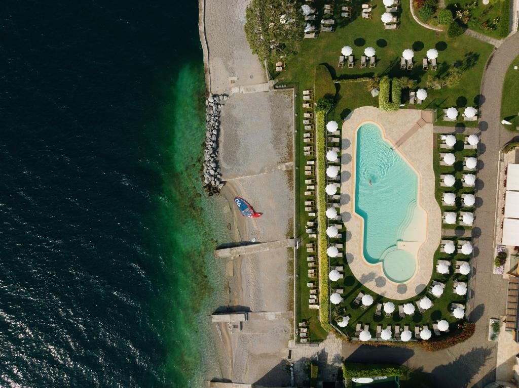 An aerial view of a resort with a large pool, beach area, and numerous outdoor seating areas.