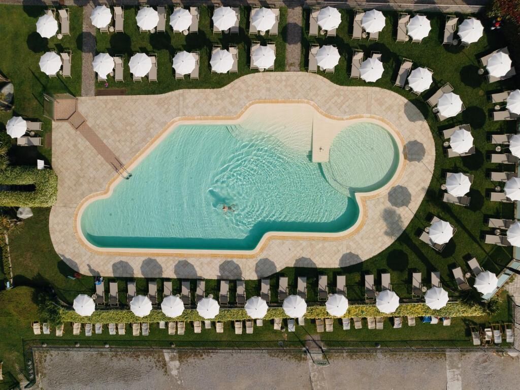 Vista aérea de un resort con una gran piscina, sillas de sol y sombrillas.