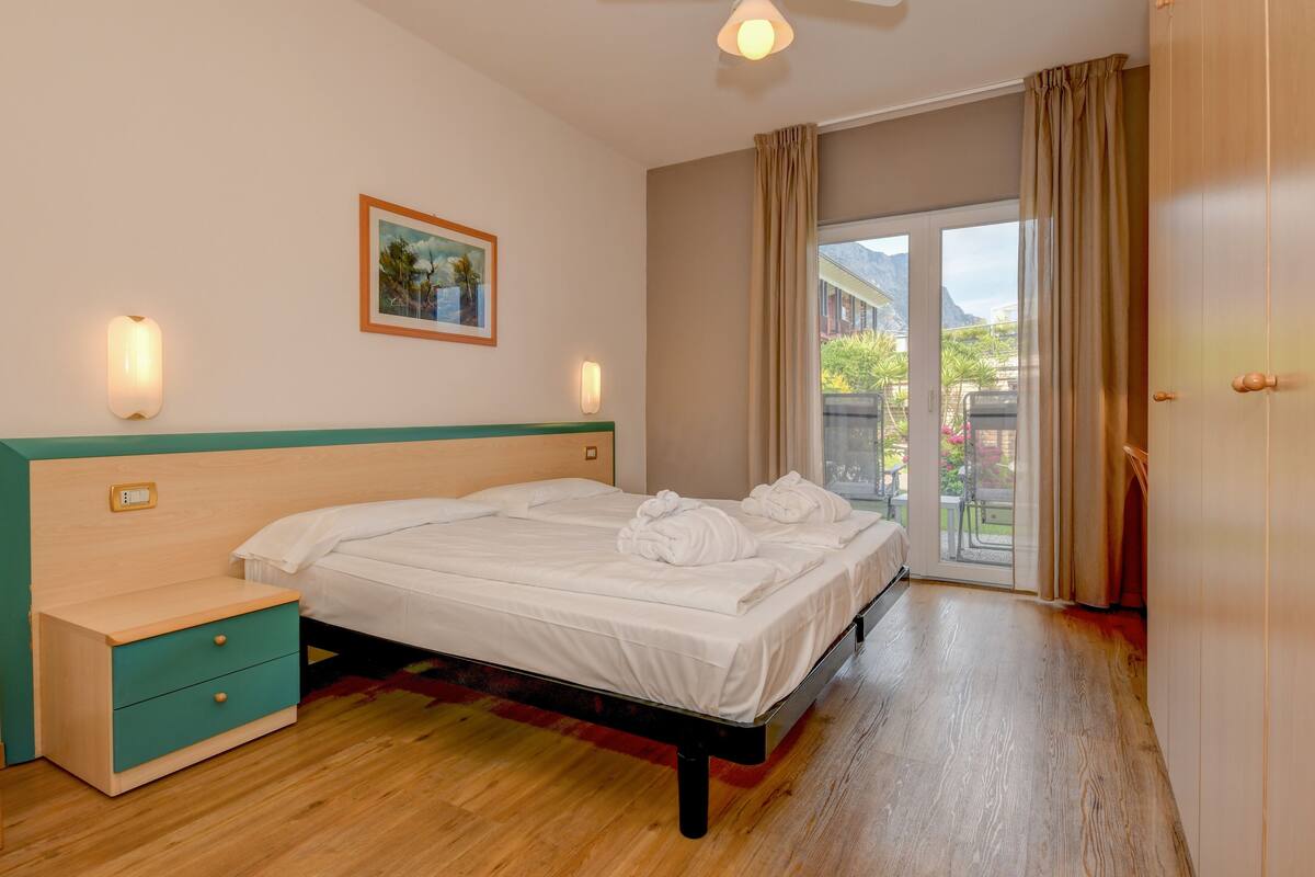 A bedroom with a bed, a nightstand, a wall-mounted light, and a window with curtains.