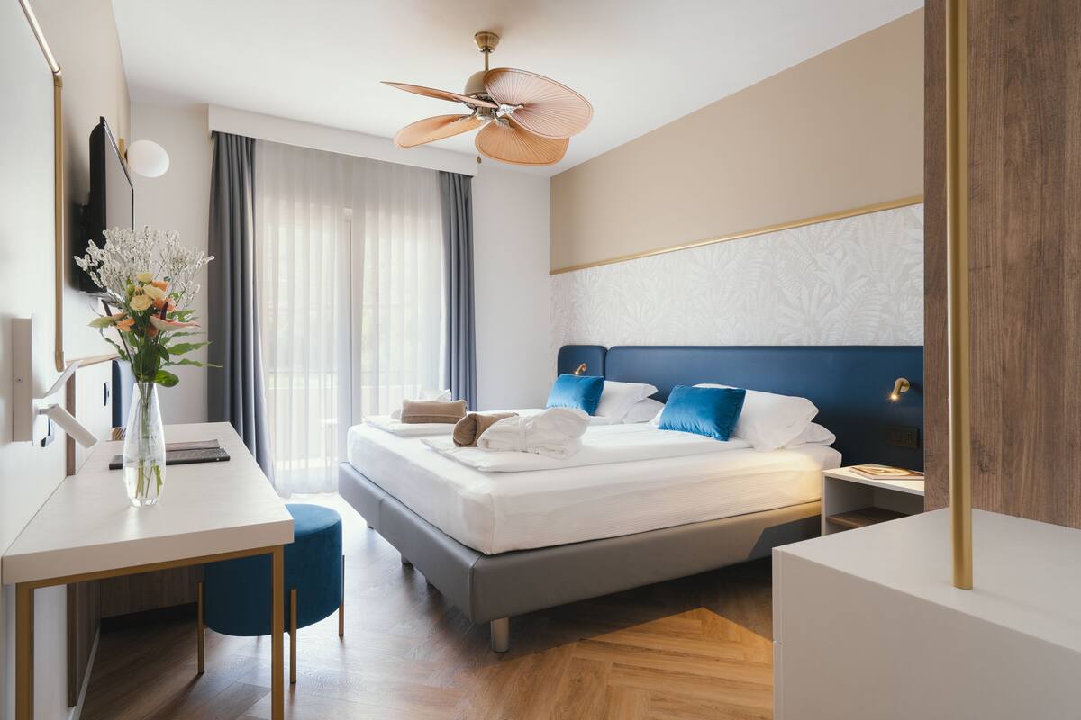 A modern hotel room with a bed, bedside tables, a desk, and a ceiling fan.