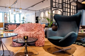 Un área de estar moderna con un sofá rosa distintivo, un sillón azul oscuro y una mesa de centro de vidrio.