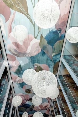 A ceiling with spherical, netted light fixtures and a floral mural. - Motel One Amsterdam (Amsterdam)