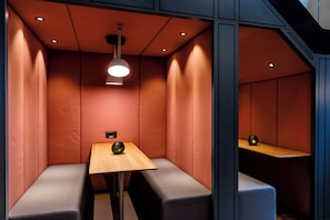 Un espacio de descanso pequeño y cerrado, con una mesa y bancos, que cuenta con iluminación empotrada y una lámpara fijada a la pared.