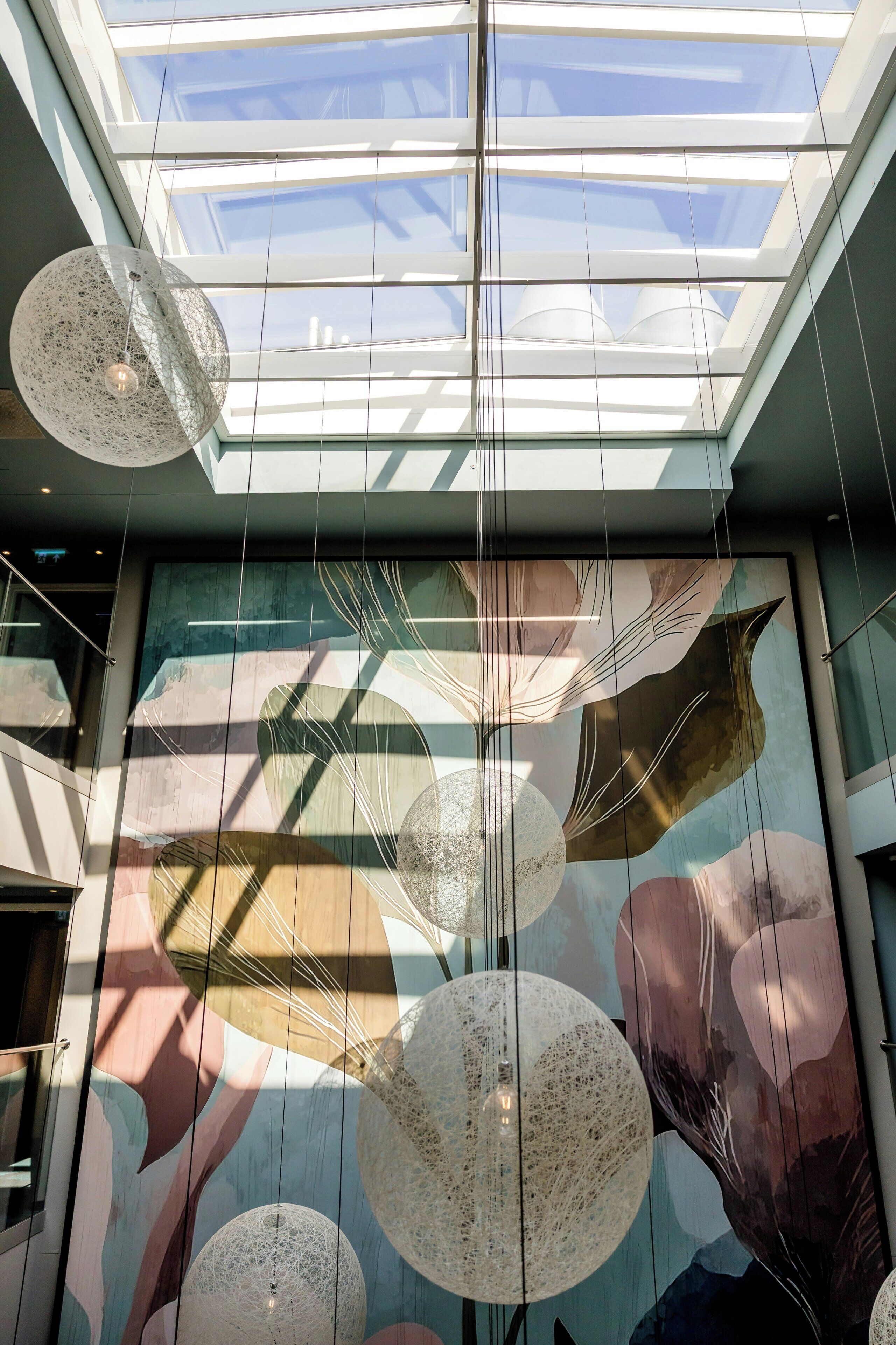 A modern interior with a skylight, abstract wall art, and hanging spherical light fixtures.