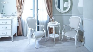 Een kamer met een witte kapstok, twee witte fauteuils, een ronde spiegel en een tafeltje met een lamp.