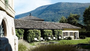 Een gebouw met een pannendak, een pergola met stoelen en een bergachtig landschap op de achtergrond.