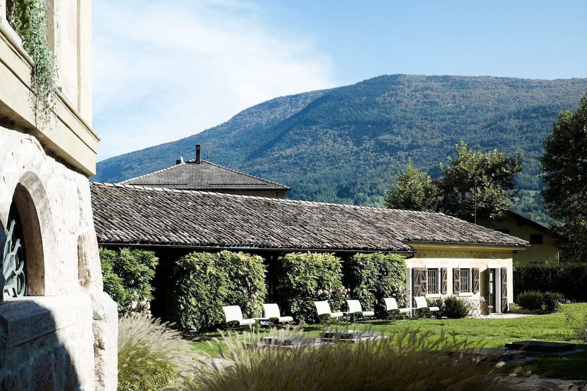 Un bâtiment avec un toit en tuiles, une pergola avec des chaises et un paysage montagneux en arrière-plan.